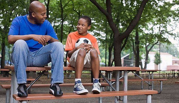 Adult and youth holding a soccer ball sitting on a bench.